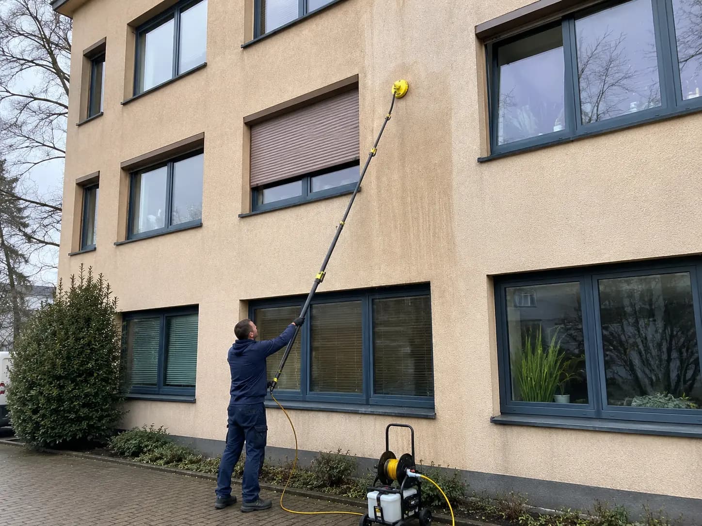 Mitarbeiter reinigt die Fassade eines Wohngebäudes in Rostock mit Teleskopstange